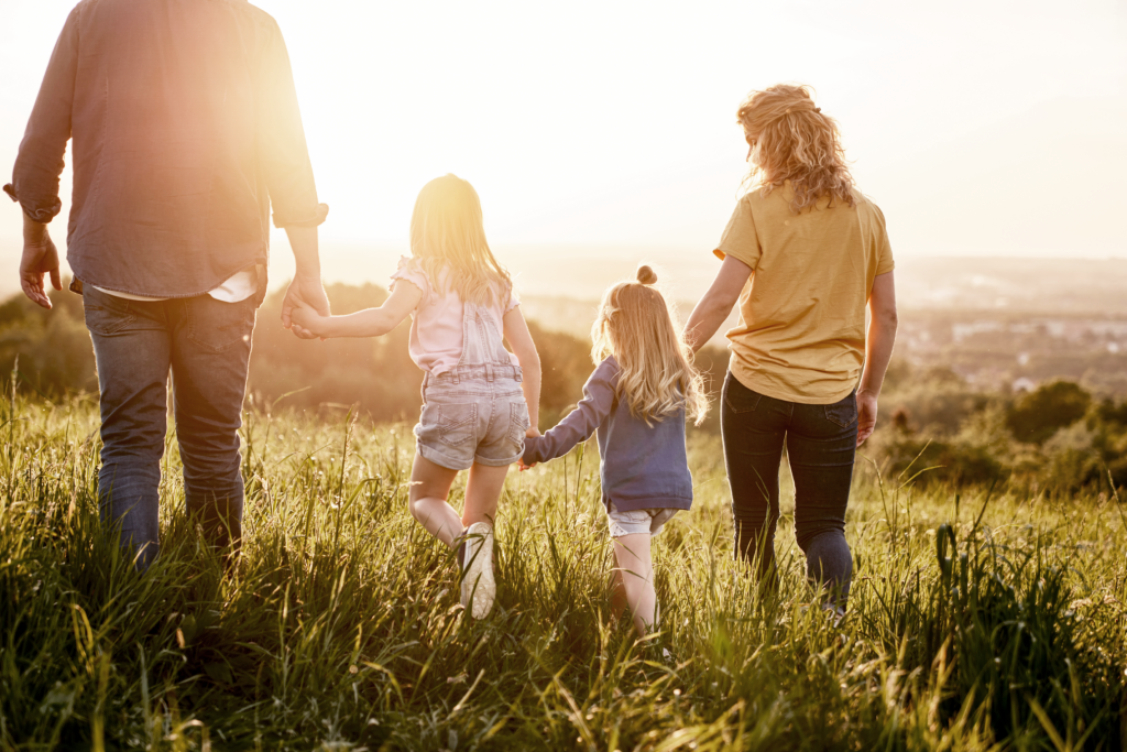 Family holding hands while walking in a field of tall grass and watching the sunset